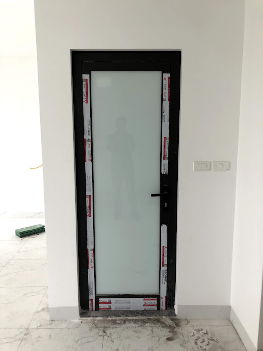 Cửa kính khung nhôm màu đen đang lắp đặt trong nhà, tay nắm cửa màu đen, nền tường trắng